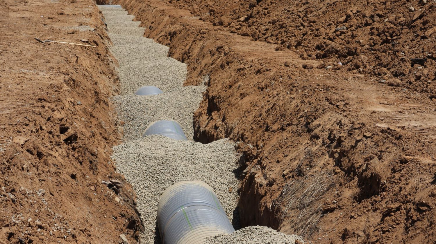 Perforated drain line resting on a gravel bed in an open trench